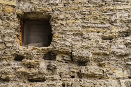 Fragment of an antique stone wall with a narrow window. Closeup.