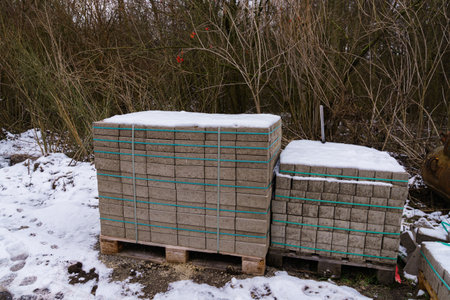 Two wooden pallets with road tiles on a snow-covered construction site.