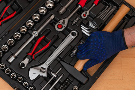 The hand of a man in a glove takes a hammer from a box with a hand tool. Top view closeup.の写真素材