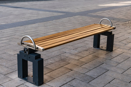 Stylish wooden bench with a metal frame on the pavement covered with stone tiles.
