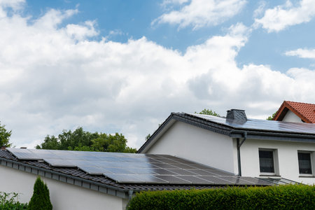 The roof of a residential building is covered with solar panels. Light white clouds in the sky.