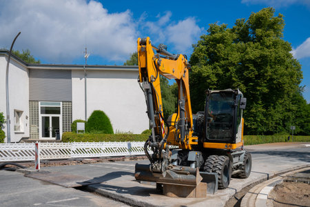 A yellow excavator sits idle on a paved road in front of a white buildingの写真素材