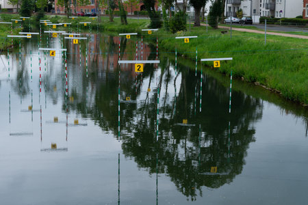 A calm river with numbered buoys marking a canoe slalom course. The reflection of trees and nearby buildings are visible in the water.View from above.の写真素材