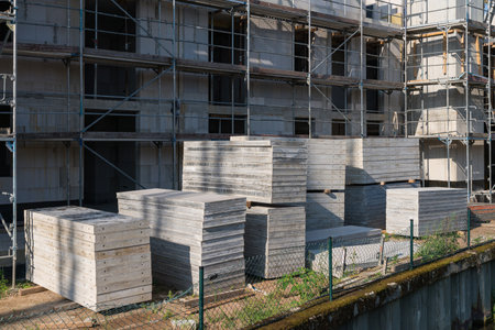 A residential building under construction surrounded by scaffolding and concrete panels stacked in...