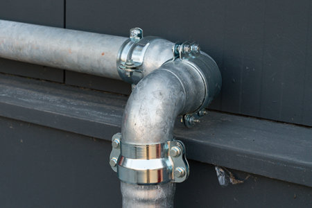 A close view of a metal plumbing pipe featuring a shiny elbow joint, attached securely to a...