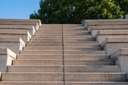 A set of wide, concrete steps ascends towards a vibrant green park. The sunlight casts shadows on...
