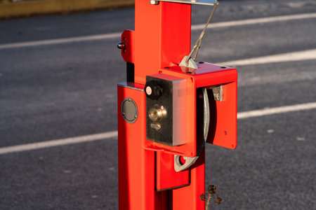 A bright red gate mechanism is affixed to a sturdy post, resting on a paved area. The device...