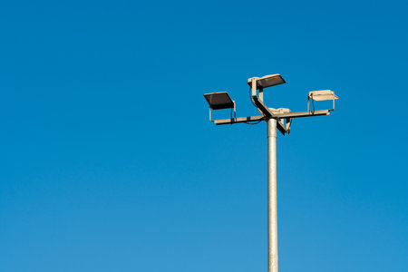 A tall pole supports multiple streetlight fixtures against a bright blue sky. The cloudless backdrop highlights the fixtures, emphasizing urban infrastructure and public safety measures.の写真素材