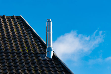 A metal chimney rises from a pitched roof, showing modern architecture. Soft clouds drift in the bright blue sky, complementing the contemporary design of the home.の写真素材