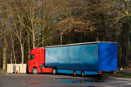 A large red truck with a blue trailer is parked in an area surrounded by trees. It is a clear sunny day, indicating a serene and quiet environment.の写真素材