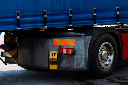 Rear view of wheel and brake light of large truck parked at a loading dock features a blue tarp covering its cargo.の写真素材