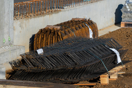 Metal rebar is stacked neatly on wooden pallets at a construction site. The bright sunlight...