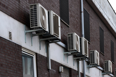 Multiple air conditioning units are installed outside a residential building's wall. These units...
