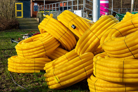 Coiled yellow hoses are stacked outdoors at a construction site during early spring. Nearby structures and tools indicate preparation for upcoming work in the area.の写真素材