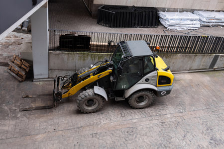 Yellow construction forklift stands on construction site. The vehicle is equipped with forks for...