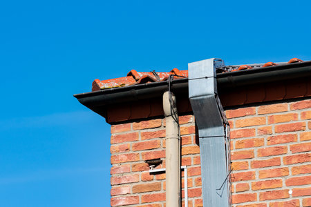A close-up view of a brick building's corner shows a section of the roof and a silver downspout...