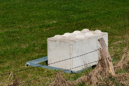 A concrete block is placed on a grassy area, secured by a metal frame, next to a barbed wire fence....