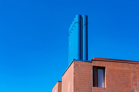 A striking blue chimney rises from a contemporary brick structure, contrasting with a bright blue sky. The architectural design showcases a blend of textures and colors, creating visual interest.の写真素材