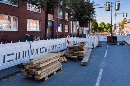 A construction site is visible with stacked wooden planks on the ground. Barriers line the street, while bicycles are parked nearby.の写真素材