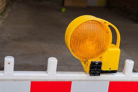 A bright yellow warning light sits atop a white barricade with red markings at a construction site....