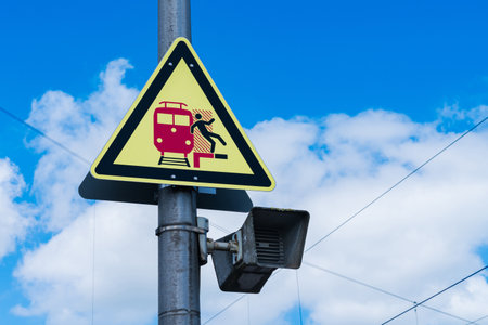 A triangular warning sign displays a train and a person stepping back, urging caution. The bright colors stood out against a blue sky with fluffy clouds, emphasizing safety near railway tracks.の写真素材
