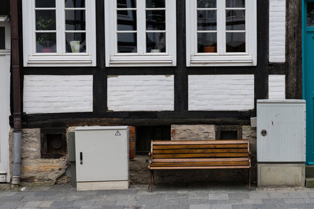 A wooden bench sits against a white and black timber-framed building. The architectural style reflects the character of the neighborhood. Nearby, utility boxes are integrated into the scene.の写真素材