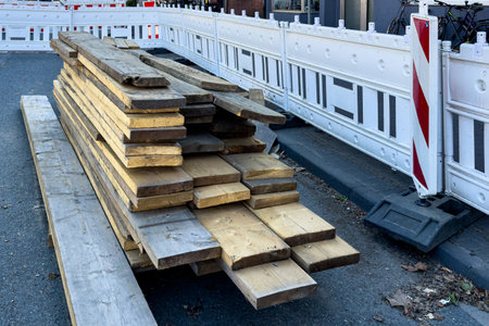 Various wooden planks are neatly stacked on a city street near a construction site, surrounded by a temporary barricade. The area appears to be undergoing renovations, indicating active work.の写真素材