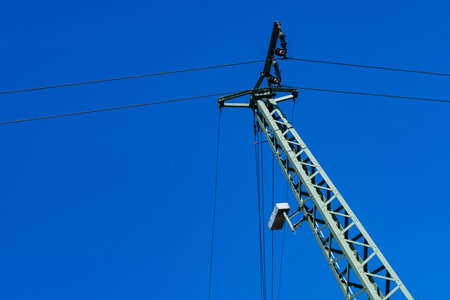 A tall powerline tower reaches upward against a vibrant blue sky.の写真素材