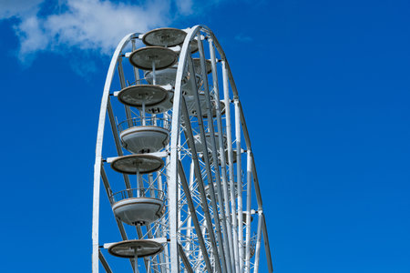 The towering structure of a Ferris wheel stands prominently against a clear blue sky. Its iconic cabins are visible, inviting visitors to enjoy a scenic view. A perfect day for outdoor fun.の写真素材