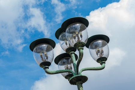 A group of vintage street lamps stands tall against a vibrant blue sky adorned with white clouds. The ornate design and clear glass create a charming urban atmosphere, evoking nostalgia.の写真素材