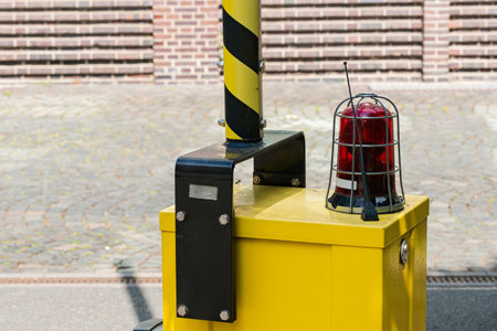 A yellow barrier stands prominently on a city street, equipped with a red warning light on top. The...