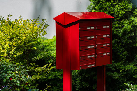 A vibrant red mailbox stands tall amidst lush green bushes and trees. Close up.