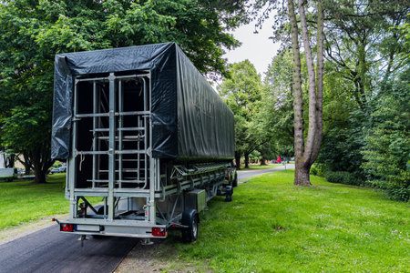 A trailer covered with a tarp is parked along a winding path surrounded by lush green trees. The scene captures a peaceful moment in a nature-filled environment during daytime.の写真素材
