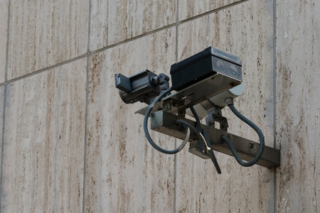 A surveillance camera is mounted on a concrete wall, featuring a textured surface. The camera's lens...