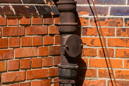 A close-up view of a rusty pipe mounted on a textured orange brick wall. The setting reflects an urban environment, showing signs of aging and industrial charm.の写真素材