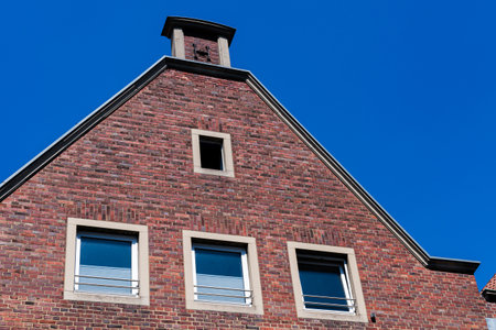 A red brick building features a triangular roof topped with a chimney against a vivid blue sky.の写真素材