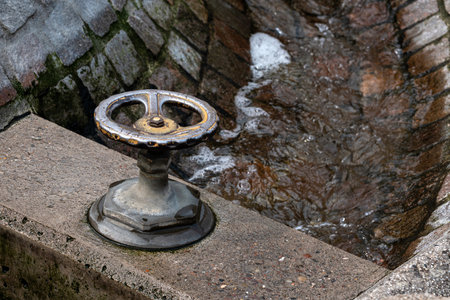 A metal water valve sits at the edge of a brick-lined canal, with water flowing through.の写真素材