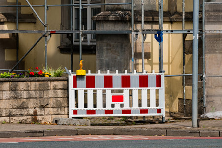 A construction site shows scaffolding and a barrier preventing entry. Flowers bloom near the wall, adding color to the area.の写真素材