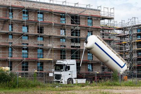 A construction site features a white cement tanker truck positioned next to a building. The truck is pouring material while scaffolding surrounds the structure, indicating ongoing development.の写真素材