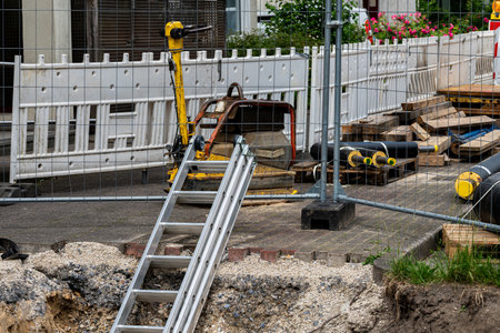 A construction site features a ladder leaning against a fenced area. Nearby, various equipment and materials are organized, indicating ongoing work in the urban location during daylight hours.の写真素材