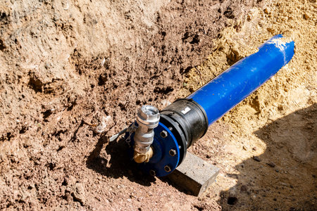 A blue water pipe is being installed in a trench. The equipment displays a valve connected to the...