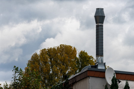 A tall chimney rises above a suburban building, accompanied by a large satellite dish. The sky is...