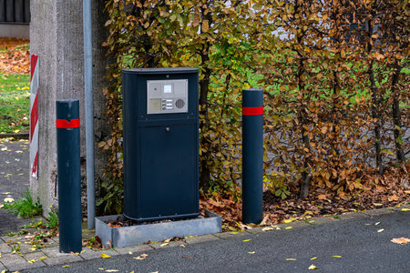 A modern intercom on the gate against a backdrop of vibrant autumn leaves. Two poles with red...