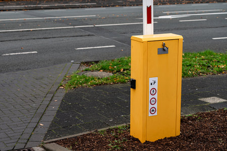 A bright yellow barrier box is positioned next to a paved sidewalk in an urban setting. Green grass surrounds the area, and a quiet road is visible in the background.の写真素材