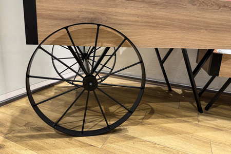 A stylish wooden table features a black metal wheel partially visible underneath. The scene captures a contemporary interior design, showing clean lines and warm tones.の写真素材