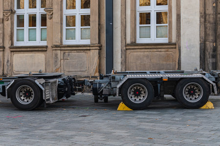 A truck chassis stands parked on a cobblestone street next to old historic buildings. The vehicle's...