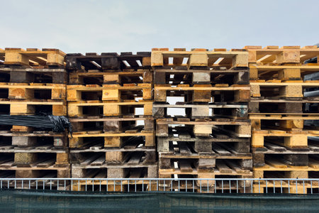 A large number of wooden pallets are stacked neatly against each other in a storage area. The scene is illuminated by natural daylight, highlighting the textures of the wood.の写真素材