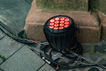 A round stage red led light sits on the ground next to a stone wall. The light is turned on, showing...