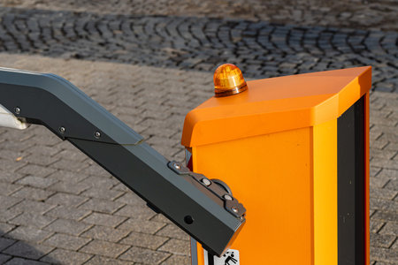 A traffic barrier system is seen in a city setting. The barrier arm is in the down position, and a...