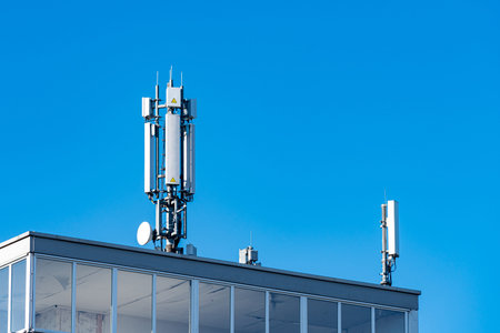 Two telecommunication towers stand on top of a building under a clear blue sky. The towers are...